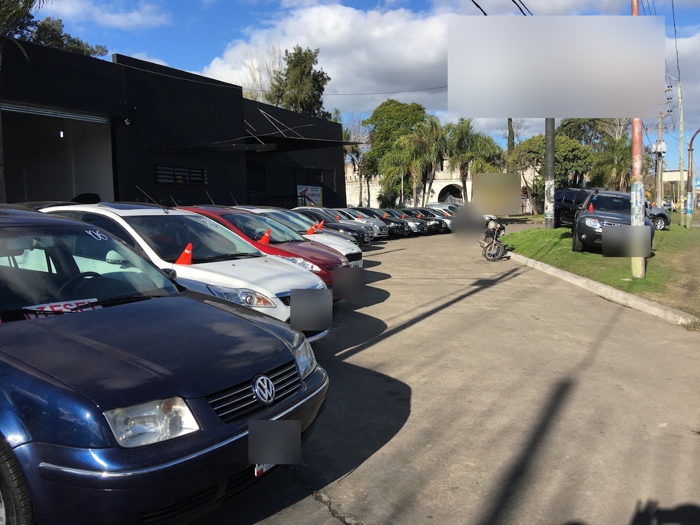 Hilera de autos usados frente al local de la concesionaria en tu zona, con el cartel alto sobre la Av. •••••