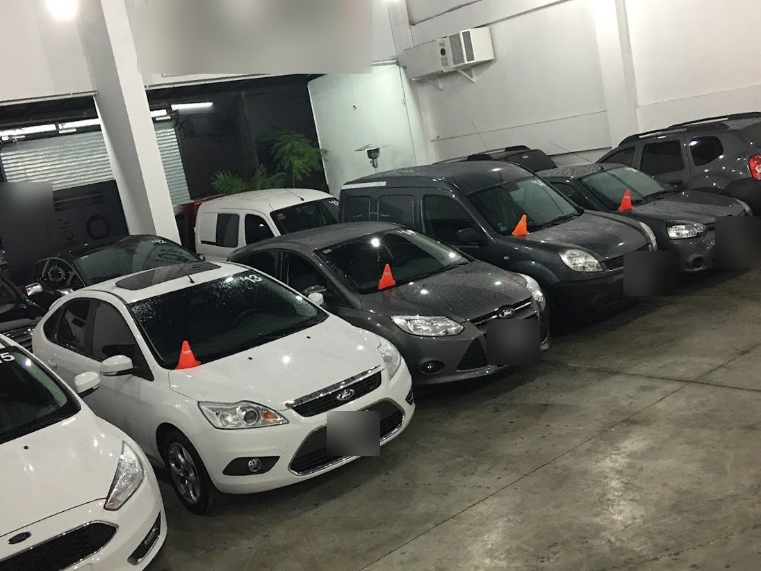Salón cubierto de la concesionaria en tu zona con Ford Focus, Renault Kangoo y Duster en fila, cada uno con un cono naranja sobre el capot