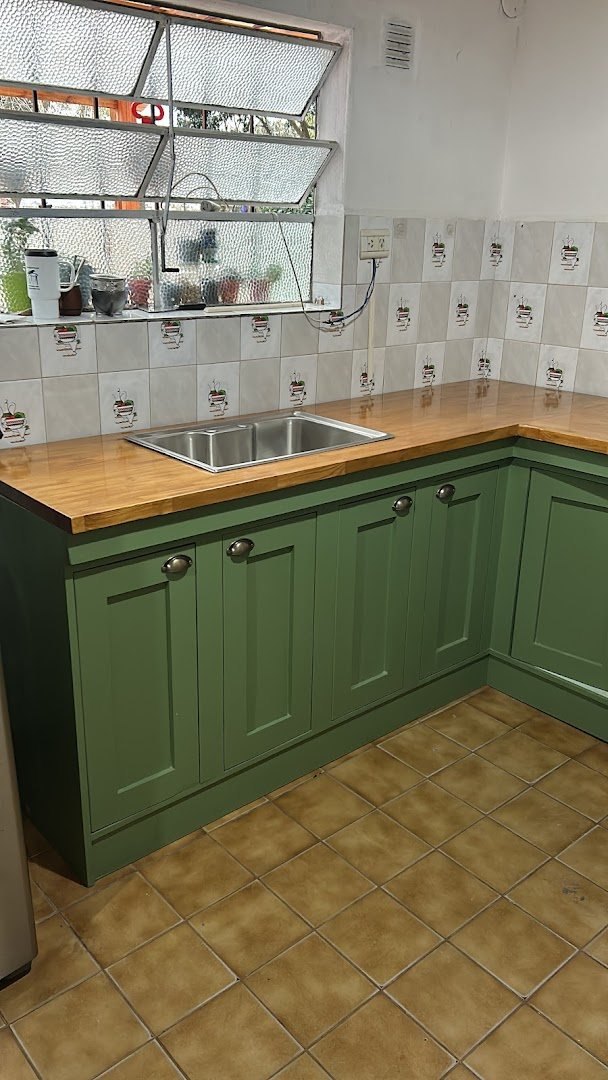 Cocina en L pintada de verde, con mesada de madera y pileta de acero, instalada en una casa