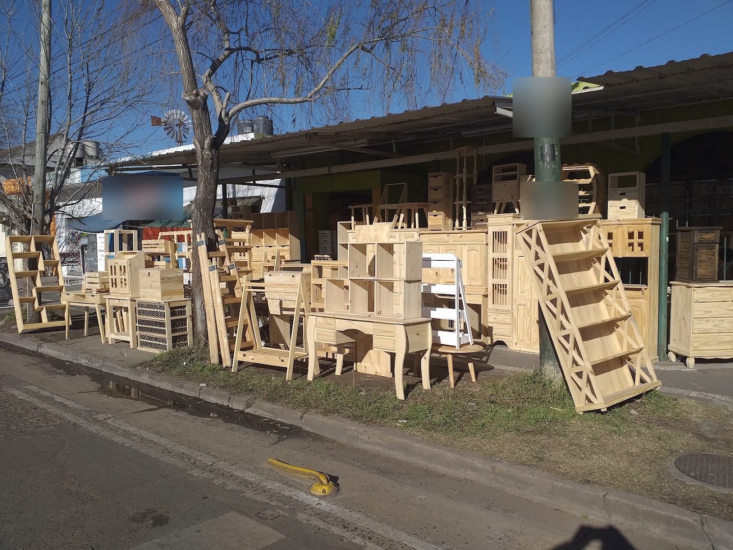 El frente del local sobre la vereda, con muebles de pino terminados en exhibición bajo un sauce