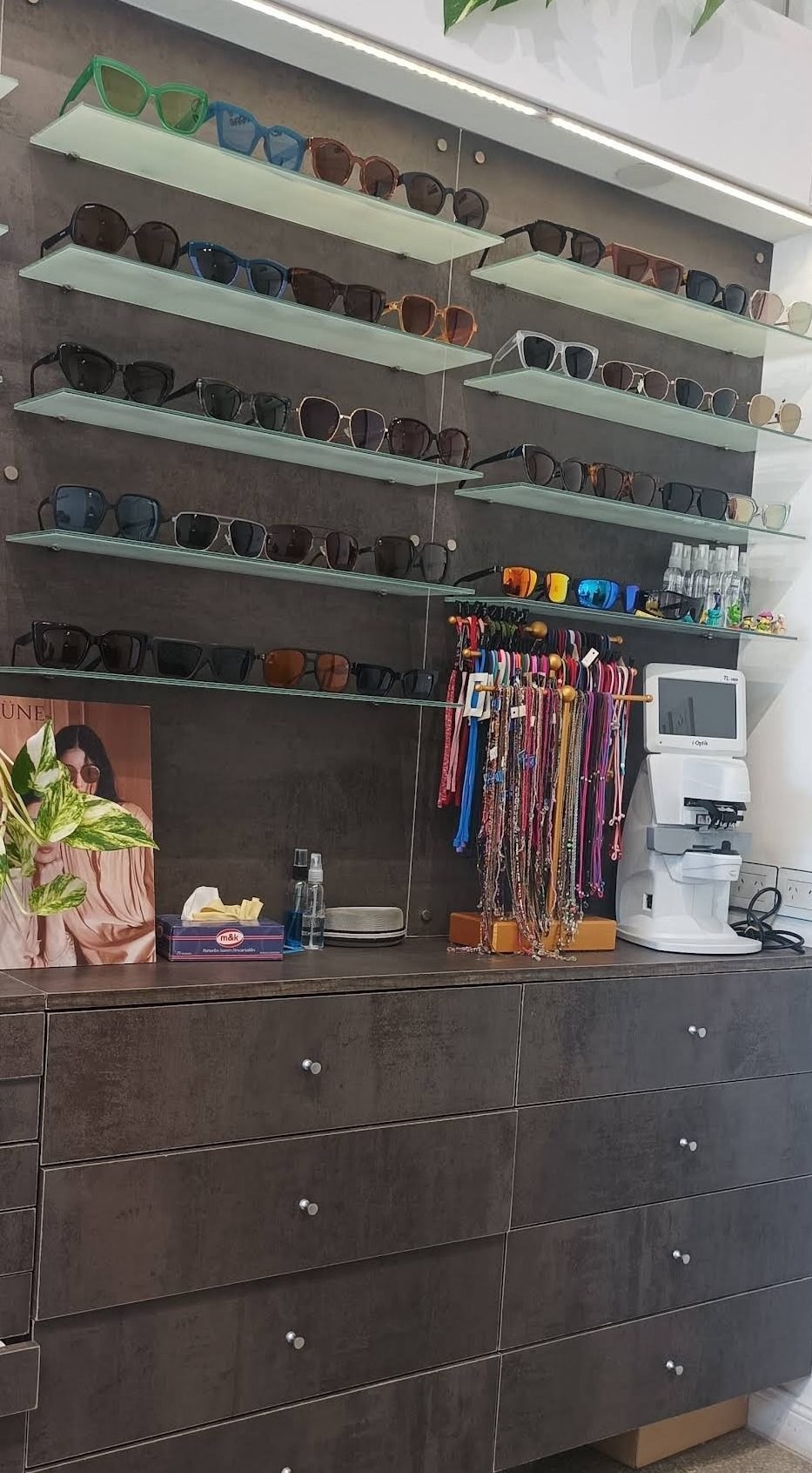 Pared de lentes de sol de colores en la óptica, tu zona, con cordones para anteojos colgados al costado