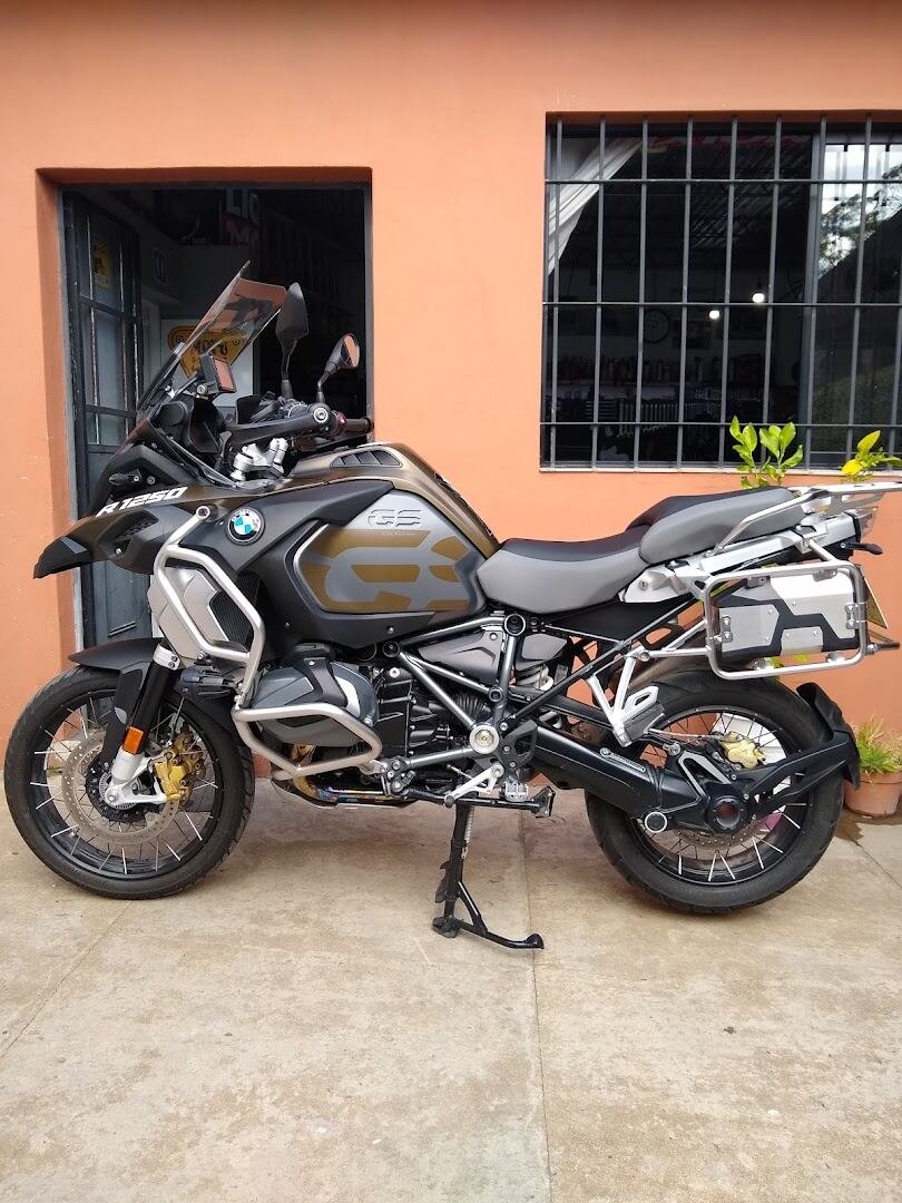 BMW R1250 GS Adventure estacionada frente al frente naranja del local, con la ventana del local de fondo, en tu zona