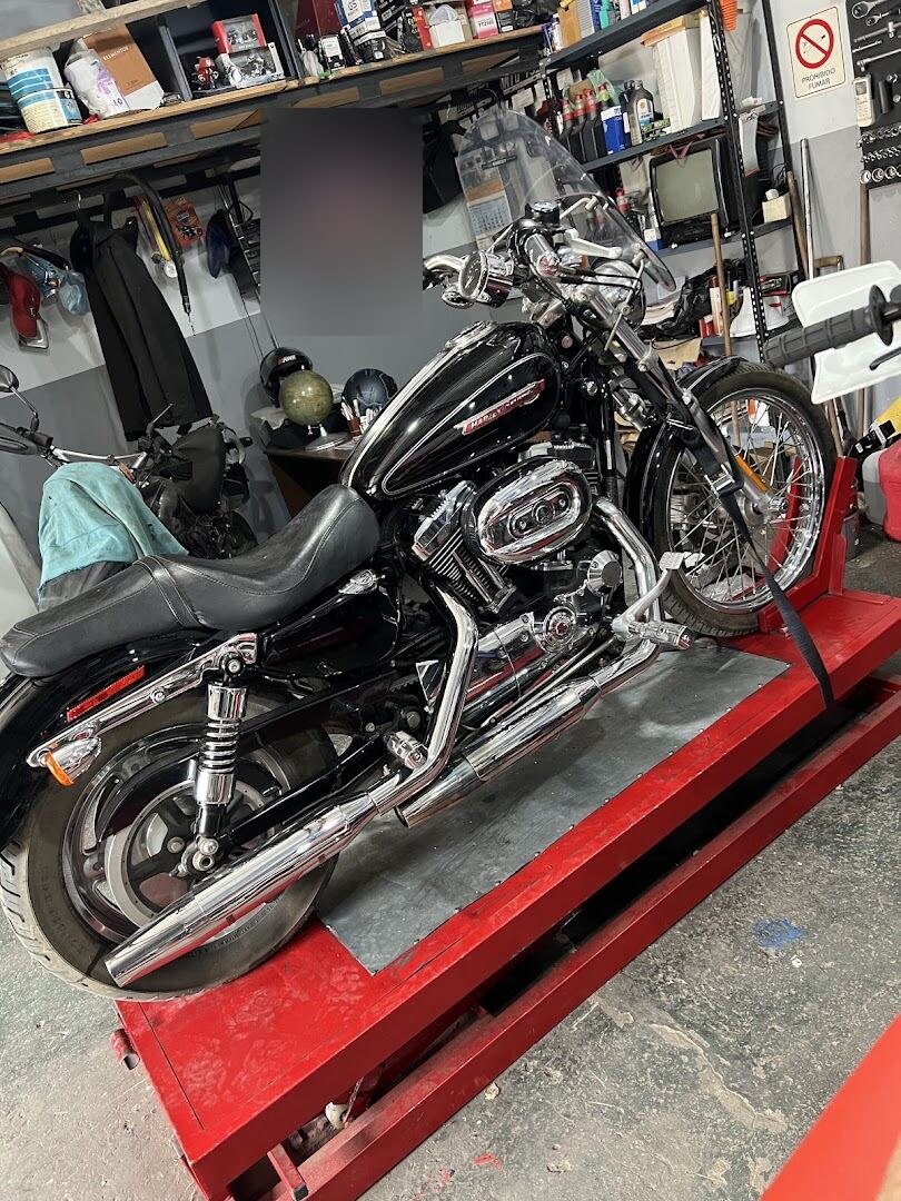 Harley-Davidson Sportster negra montada en el elevador del taller, con un cartel de Liqui Moly de fondo, en tu zona