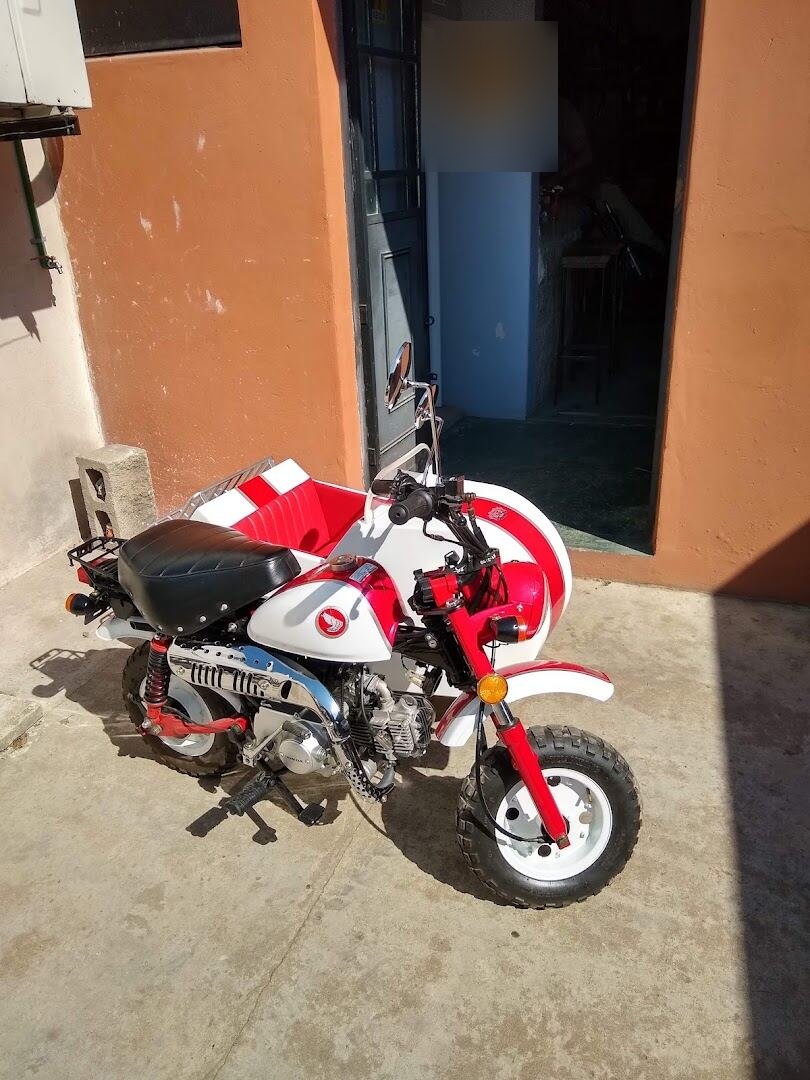 Honda Monkey roja y blanca con sidecar a medida, estacionada en la puerta del taller