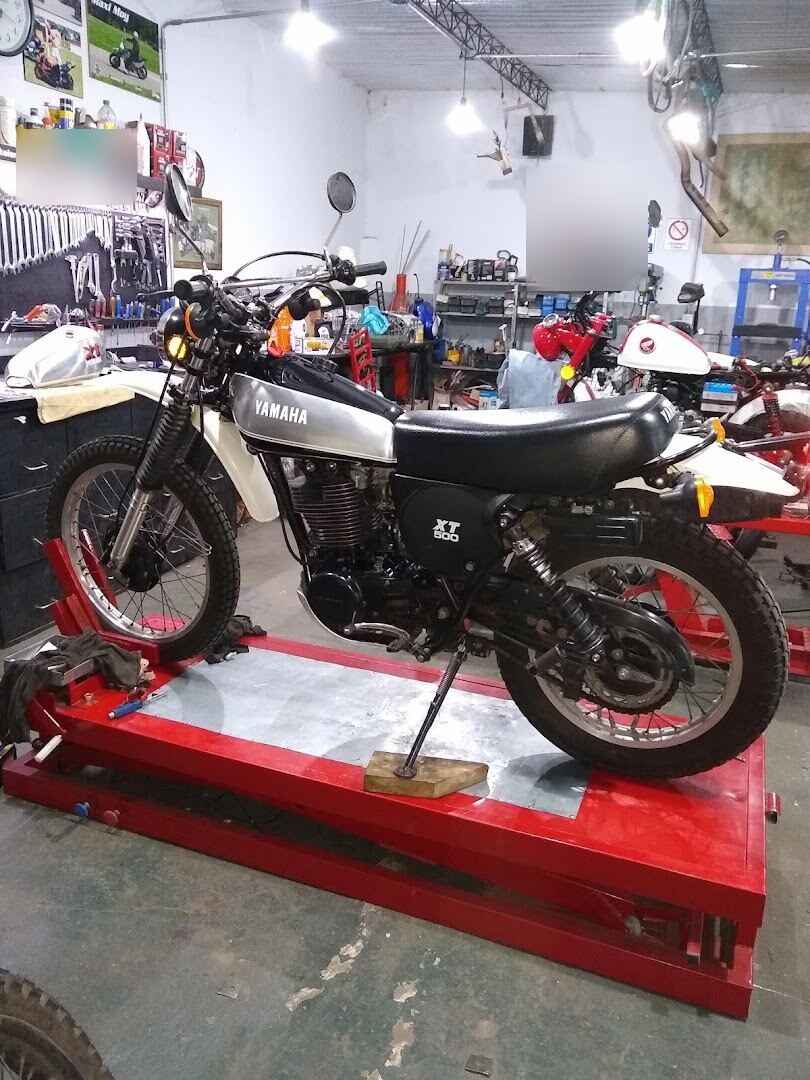 Yamaha XT500 clásica, blanca y negra, apoyada en el caballete sobre la mesa elevadora del taller